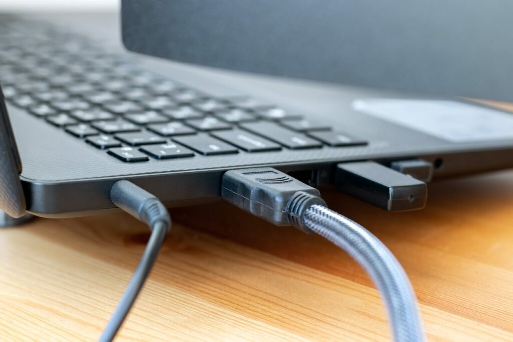Two cords are plugged into a laptop on a wooden desk.