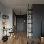 A tidy, organized studio apartment with a desk and chair against a white wall.