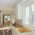 A kitchen sits empty in the middle of a renovation. The countertops have been removed and white cabinets hang on the walls.