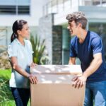 A man and woman move a cardboard box on a sunny day