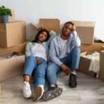 A man and woman sit looking exhausted in front of moving boxes