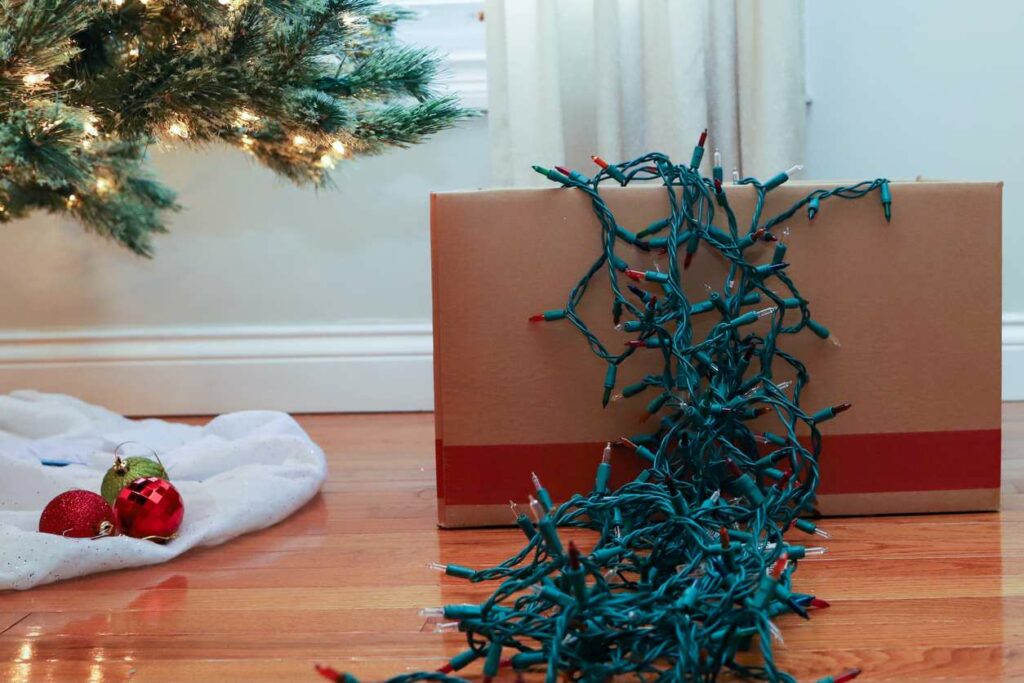 String lights are draped over a cardboard box next to a Christmas tree.
