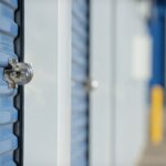 A line of storage units with blue doors sit locked with disc locks