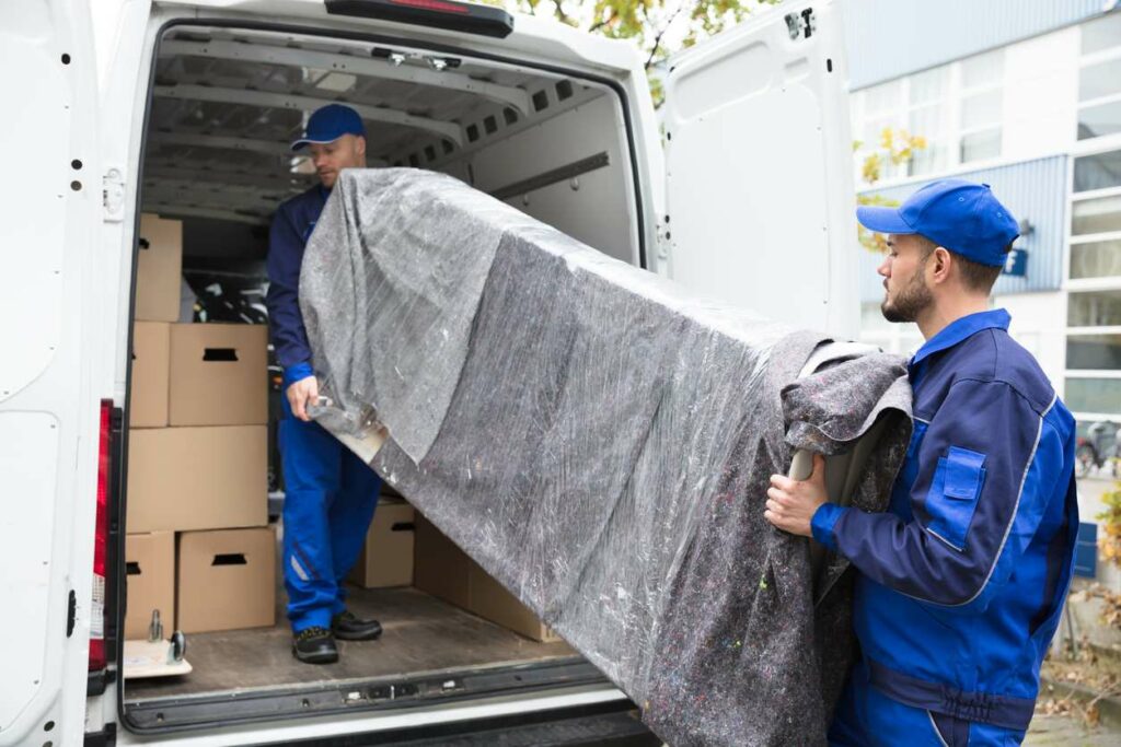 Two movers loading a wrapped piece of furniture into a van