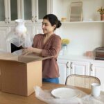 Woman wrapping and putting dishes in a cardboard box.