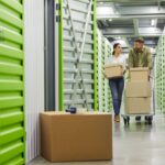 Two people moving a hand cart and boxes through the hallway of a self storage facility.