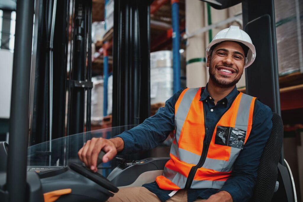 Forklift driver sitting in vehicle in warehouse smiling looking at the camera.